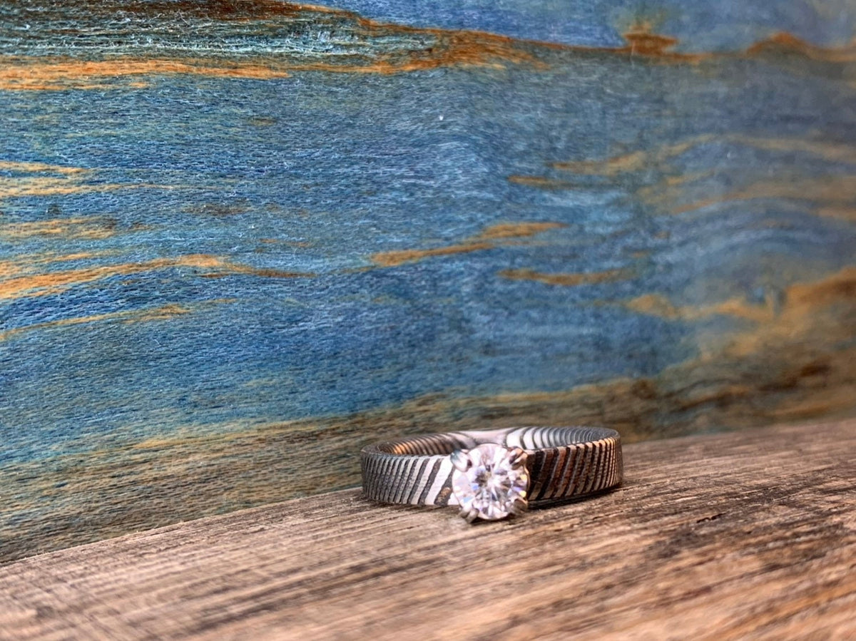 Ladies Moissanite Damascus steel engagement ring with intricate pattern and sparkling stone from RobandLean's rings collection.