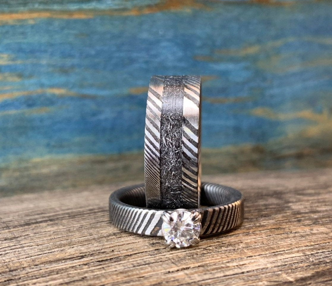 Damascus steel wedding band set with meteorite accents and moissanite gemstones, crafted by RobandLean's rings.