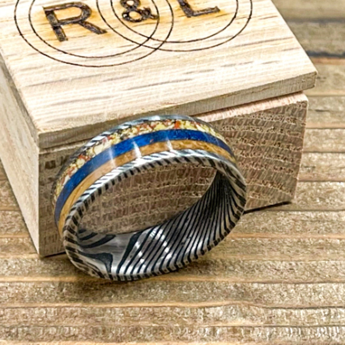 Damascus steel wedding band with dino bone, blue box elder wood, and whiskey barrel wood, by RobandLean's rings.