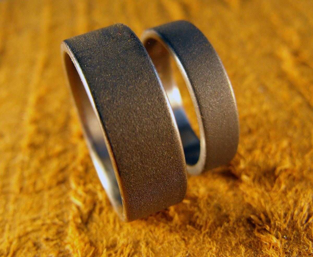 His and hers titanium wedding bands set by RobandLean's, custom-made couples rings with engraved detailing, on a neutral background.